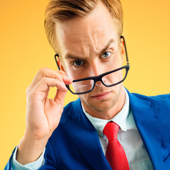 Are you seriously?! Portrait of funny skeptic businessman in corporate style blue suit and red tie, looking through glasses, over yellow-orange color background. Business concept.