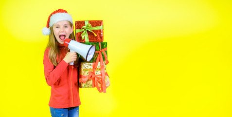 Girl in santa claus hat with box boxes in hand shouts into a megaphone, on a yellow studio background. Sales time