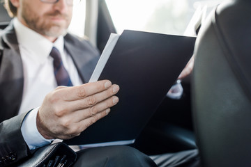 selective focus of bearded diplomat holding folder in car