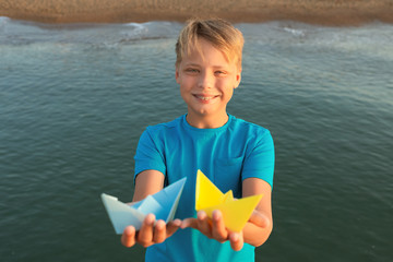 Closeup view of cute handsome white kid holding two paper bright blue and yellow colors ships...
