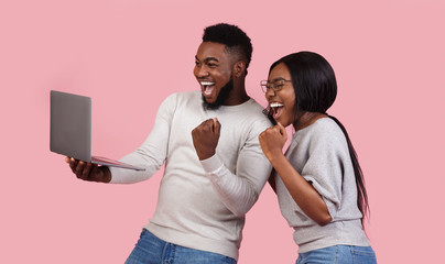 Happy black couple celebrating success with laptop