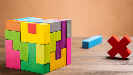 Missed items are seting in the colorful wooden cube puzzle on the brown table. Geometric shapes on a wooden background.