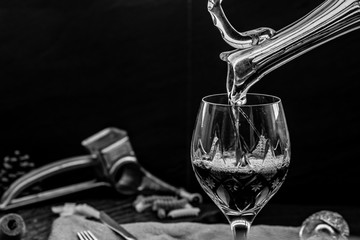 Black and white picture of Pouring red wine from pitcher into the wineglass : traditional...