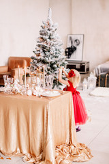 New Year 2020. New Year mood. Table with a gold tablecloth, decorated with candles and tableware for celebration. Festive still life by candlelight. The child hangs the ball on the Christmas tree.