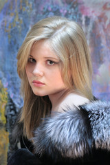 Portrait of a pensive teenage girl, a natural blonde with long hair in a chic silver fox fur coat