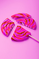 Pink Lollipop split into pieces on a pink background, top view, close-up.