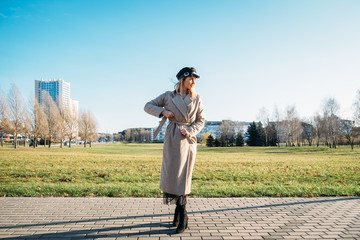 Young stylish girl in a beige coat, in a black cap, in heels. walking the city.