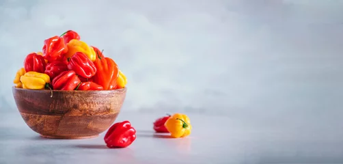 Fotobehang Chili Pepers Yellow and red scotch bonnet chili peppers in wooden bowl over grey background. Copy space.  © jchizhe