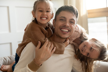 Funny father and two kids daughters embracing looking at camera