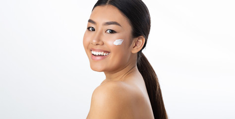 Pretty asian girl applying moisturizer cream on face