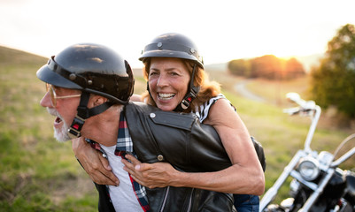 A cheerful senior couple travellers with motorbike in countryside.