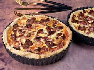 Homemade quiche with chanterelles and bacon, on brown background