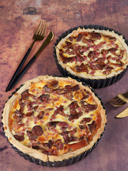 Homemade quiche with chanterelles and bacon, on brown background