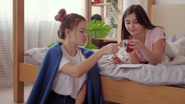 Classmates relationship. Assistance care. Teen girl using tablet helping friend in studying offering tea.