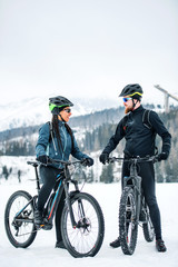Two mountain bikers with bicycles resting outdoors in winter.