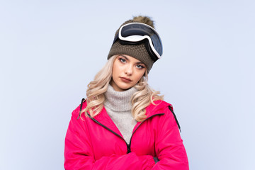 Skier teenager girl with snowboarding glasses over isolated blue background keeping arms crossed