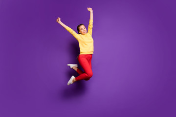 Fototapeta na wymiar Full length photo of pretty teen lady jumping high celebrating vacation time raising hands up wear casual yellow pullover red pants isolated purple color background