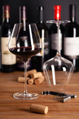 Crystal shiny glass of red wine, bottles, corkscrew, opener, sommelier knife, transparent decanter, corks on wooden table. Closeup, vertical, selective focus side view. Concept wine magazine photo