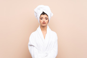 Teenager girl in a bathrobe over isolated background sad