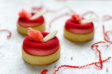 Set of contemporary raspberry mini mousse tarts covered with red velvet spray decorated with chocolate feathers on light background