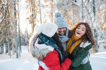 A group of cheerful young friends having fun outdoors in snow in winter forest.