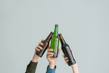 Hands clinking bottles of beer on grey background