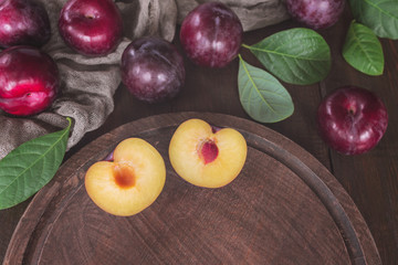 fresh purple plums and plum halves on the table top view. plums and leaves lay flat on a wooden background.