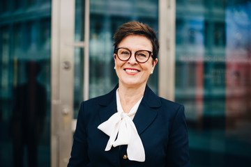 Portrait of confident smiling senior businesswoman against office
