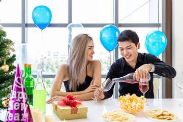 Attractive young male and female celebrate Christmas and New Year in office party, man pouring wine for woman