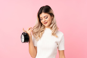 Teenager girl over isolated pink background holding vintage alarm clock