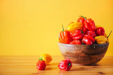 Fotobehang Chili Pepers Yellow and red scotch bonnet chili peppers in wooden bowl over orange background. Copy space.  © jchizhe