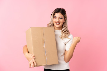 Teenager girl over isolated pink background holding a box to move it to another site