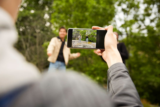 Copped image of teenage boy photographing friends dancing at park
