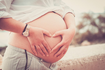 Unrecognizable new mother pregnant caucasian young woman doing hearth sign on her big beautiful...
