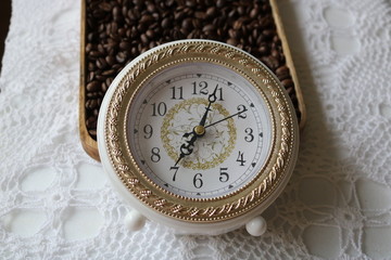 Vintage white and gold alarm clock on white vintage tablecloth next to roasted coffee beans