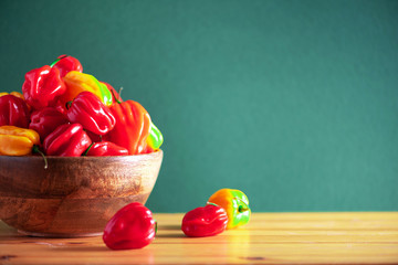 Colorful scotch bonnet chili peppers in wooden bowl over green background. Copy space.
