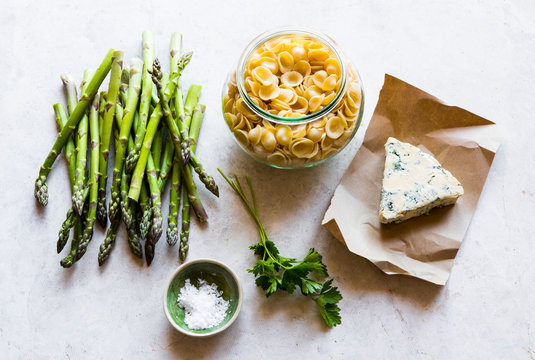 Cooking ingredients with asparagus, pasta, cheese wedge and fresh parsley