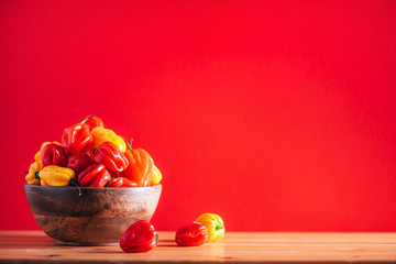 Colorful scotch bonnet chili peppers in wooden bowl over red background. Copy space.