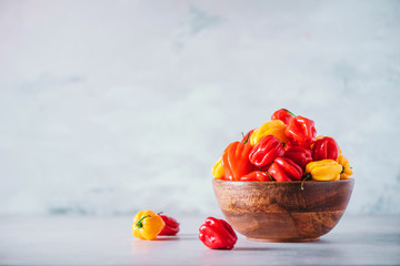 Yellow and red scotch bonnet chili peppers in wooden bowl over grey background. Copy space.