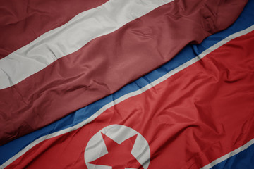 waving colorful flag of north korea and national flag of latvia.