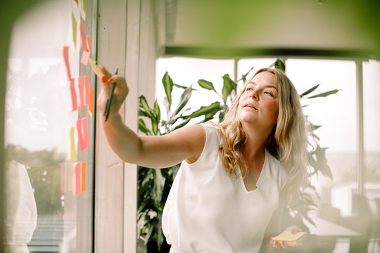 Businesswoman sticking adhesive note on glass window at convention center