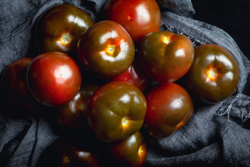 Pile of kumato tomatoes on a dark background top view.