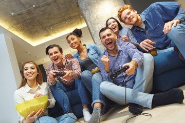 Group of friends having party indoors fun together playing football on game console