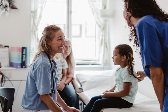 Cheerful pediatrician talking to nurse while examining girl in medical clinic
