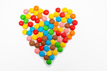 Multi-colored round candy tablets are collected in the form of a heart on a white background for Valentine's Day