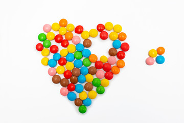 Multicolored round jelly beans collected in the form of a heart without a small piece on a white background