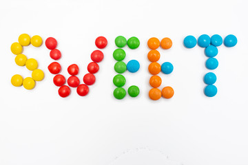 The inscription Sweet written in round small multi-colored sweets dragees on a white background