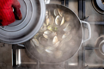 Hand in oven mitt lifting lid off pot of clams