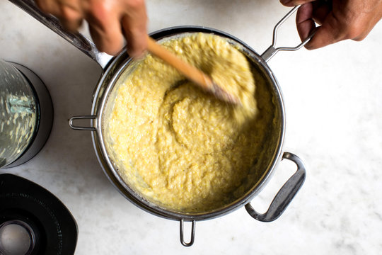 Overhead view of cook straining corn mash for soup
