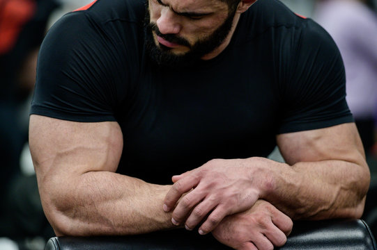 sport mental concentration concept of young strong mucle cute caucasian male with beard wearing black clothes leaning on simulator in athletic gym